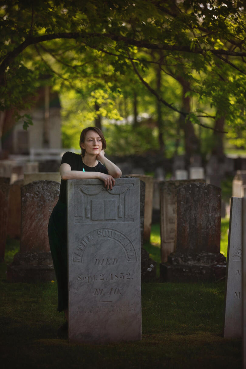 Courtney leaning on a headstone in a cemetery, there's an engraved book on the headstone.